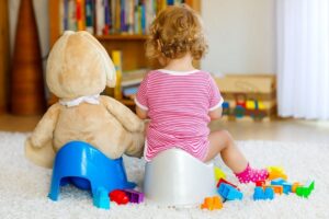 Closeup of cute little 12 months-old-toddler-baby-girl-child-sitting-on-potty.-Kid-playing-with-big-plush-soft-toy-cm