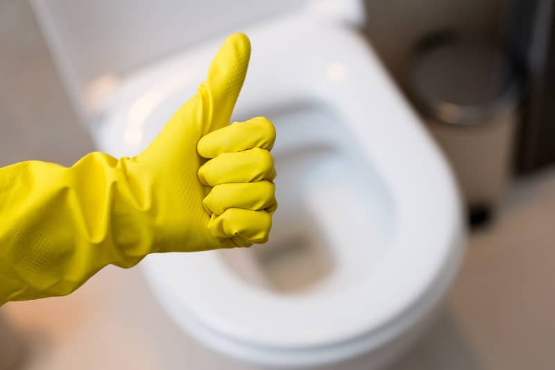 Hand with glove showing thumb up sign against clean toilet-cm