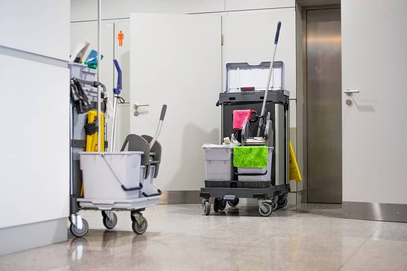 Photo of cleaning cart with tools and buckets standing near restroom door at airport -cm