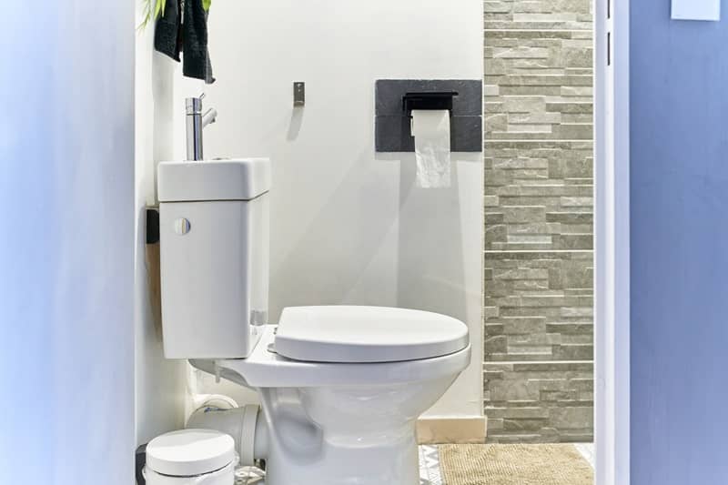 Intelligent white toilet with a washbasin on top, a wastebasket next to it and toilet paper on the wall, seen from the bathroom entrance. -cm